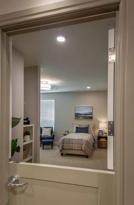 Looking into a studio apartment with natural light, extra seating, and a cozy bed